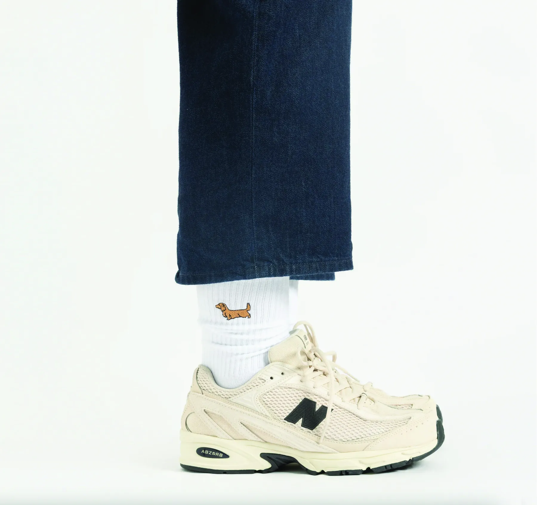 White sock with an embroidered dachshund, worn with dark denim and cream trainers